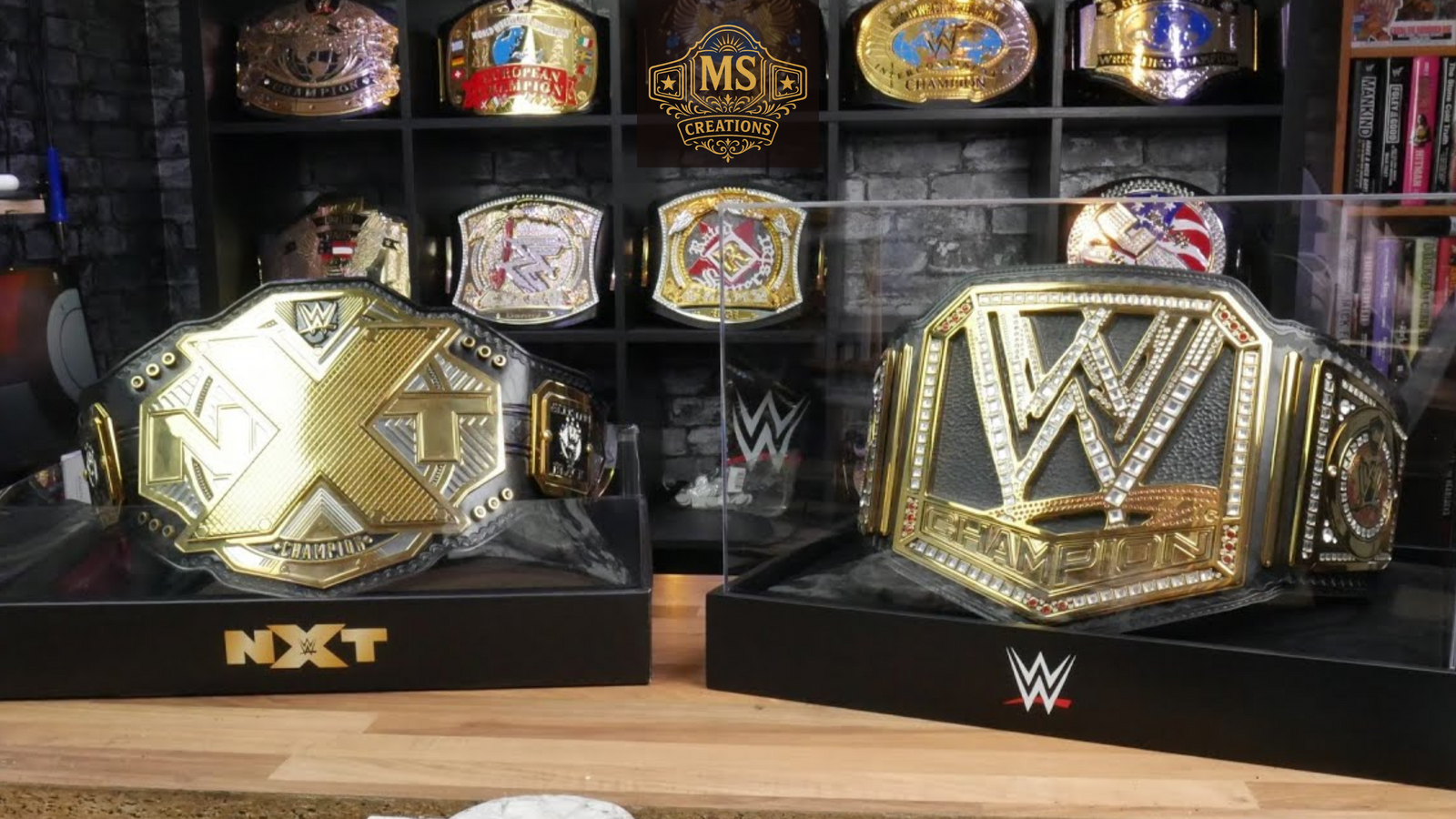 A championship belt display featuring the NXT Championship and WWE Championship belts, with several other championship belts on shelves in the background.